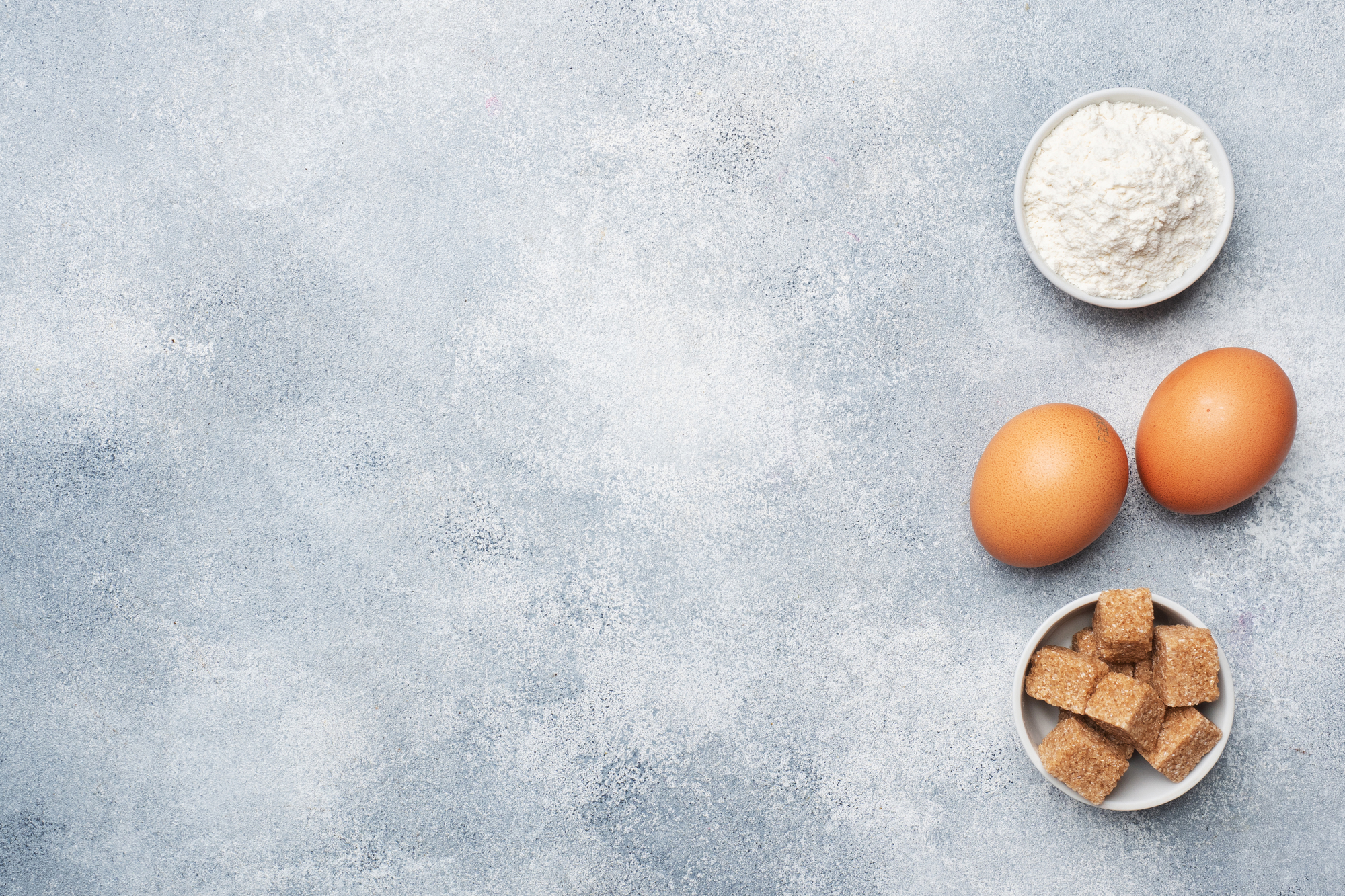 Ingredients for baking cookies, cupcakes and cake. Raw foods eggs flour sugar on a grey background with copy space.