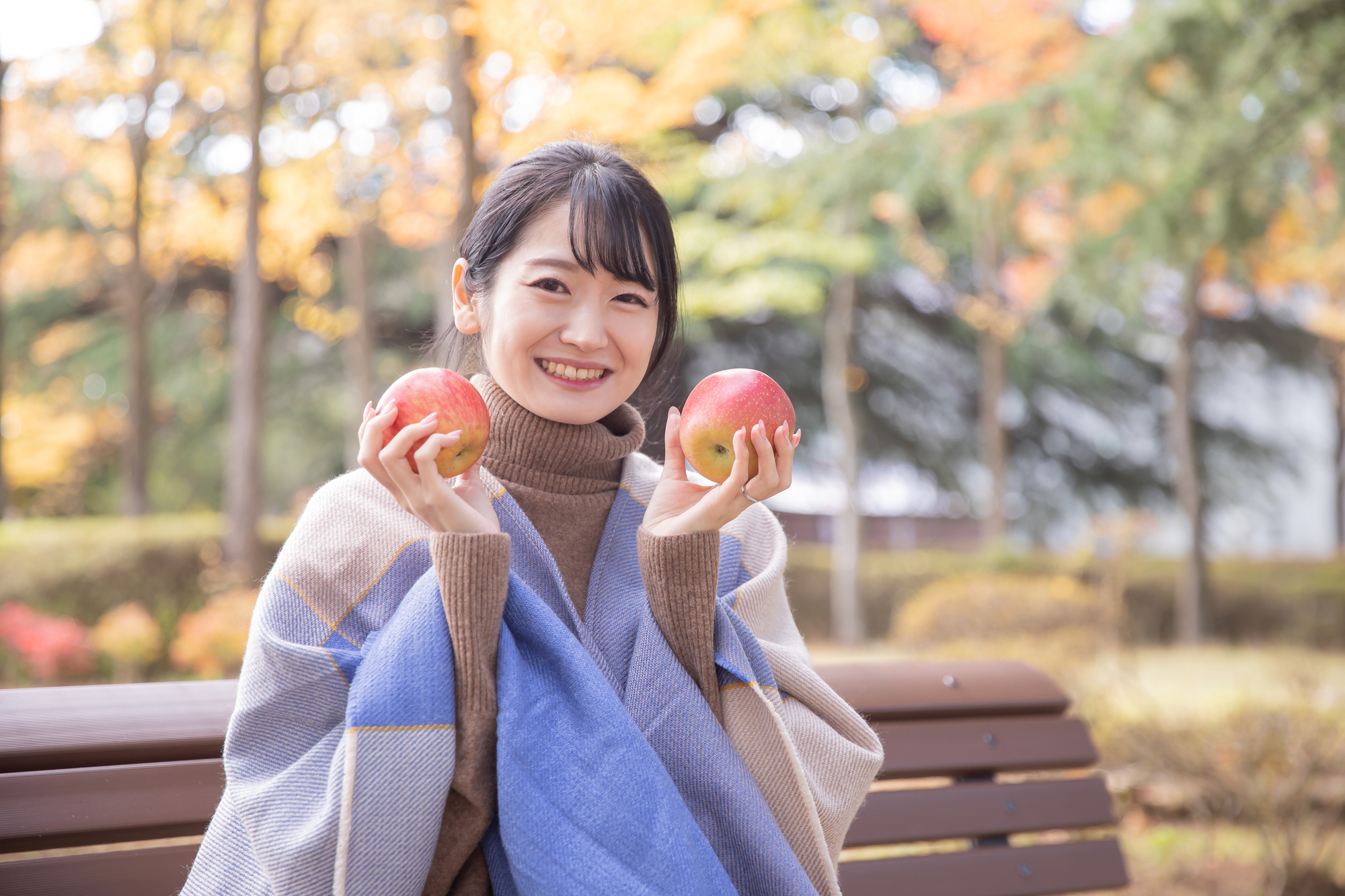 秋の公園でりんごを食べる女性