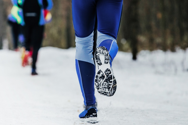 closeup legs runner and running shoes in snow winter marathon