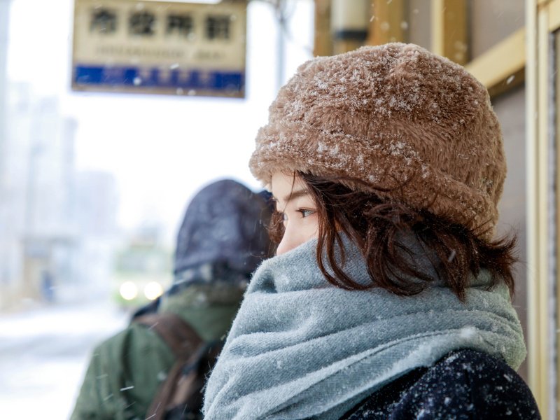 雪の降る駅で電車を待つ旅行者の女性
